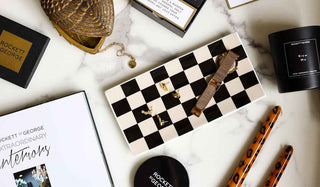 Flatlay image of gift homeware, including a 'Blow Me' Candle, Leopard Print Candlesticks, a Checkerboard Trinket Tray and the Book: Extraordinary Interiors.
