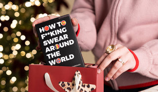 A novelty game being placed into a gift bag by a model, with fairy lights glowing in the background.