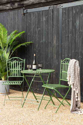 A picture of a garden with an olive green garden set with a round table and two chairs. 