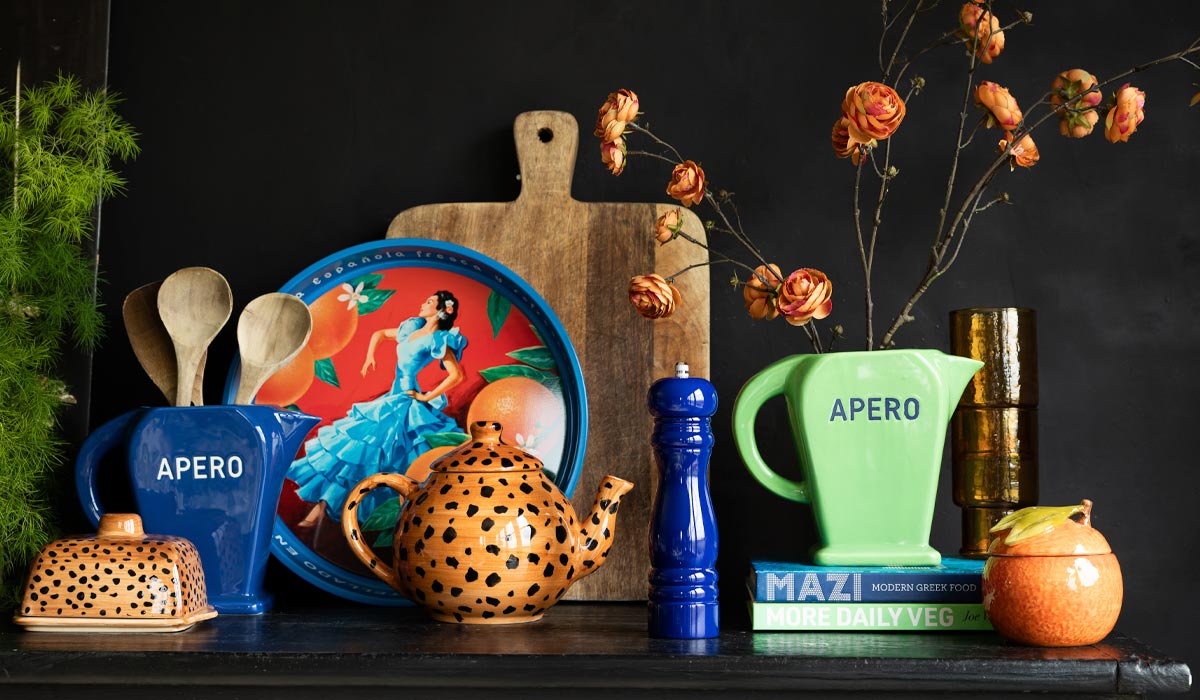 Decorative shelf with colorful kitchen items including a teapot, plates, and a pitcher on a dark background.