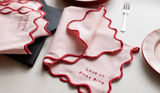 The Set of 4 Pink & Red First Bite Napkins displayed on a table with a plate, fork and serving board.