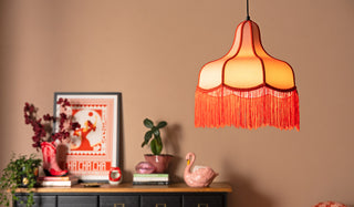 A red and pink tassel ceiling light, with a sideboard with various accessories on in the background.