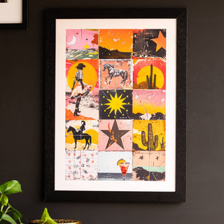 The Sunset Wild West Print displayed on a black wall, with another frame and a plant also in the shot. 