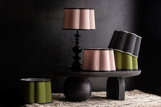 a dark and moody interior with a deep pile white rug and scalloped shape lamp shades in green, cream and black stacked on a low coffee table.