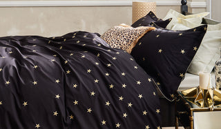 Lifestyle image of the Rockett St George Black Falling Star Cotton Bedding Set displayed on a bed styled with a leopard print cushion and various home accessories. 