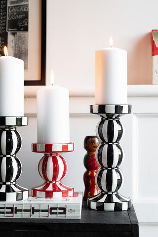 Three striped candle holders styled with lit pillar candles on, displayed on a black surface with various other accessories.