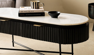 The Reeded Black Wood & Marble Low Console Table / TV Unit displayed in use in a living room as a coffee table, with books, a mug and bowl styled on the top.