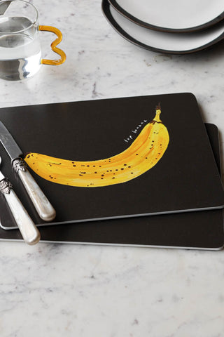 Lifestyle image of the Set of 2 Banana Placemats, styled on a surface together with cutlery, glassware and plates. 
