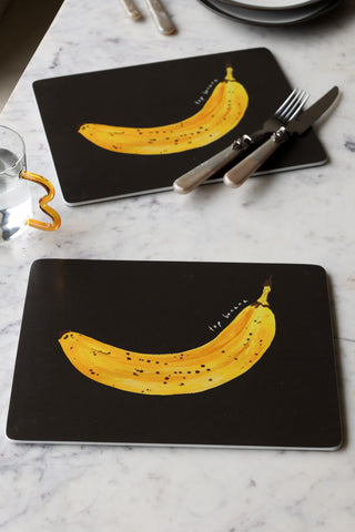 Lifestyle image of the Set of 2 Banana Placemats, styled on a white table with cutlery, glassware and plates. 