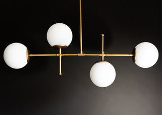 Lifestyle image of the Gold & White Glass Globe Ceiling Light hanging in front of a black wall. 
