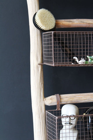 Close-up detail image of the Wooden Ladder With 5 Basket Shelves with shower brush and small monocle man ornament on dark wall background