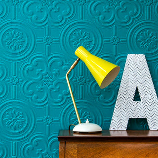 Close up of a lamp with a bright yellow shade in front of the Anaglypta Egon wallpaper painted blue - Rockett St George