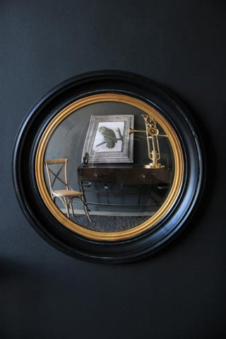 lifestyle image of black and gold framed convex mirror hanging on a dark blue wall hung on dark wall background