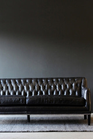 Lifestyle image of Black Leather Chesterfield 3 Seater Sofa on grey rug and dark wall background