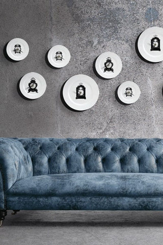 lifestyle image of clock plate clock on distressed grey wall above blue suede look sofa