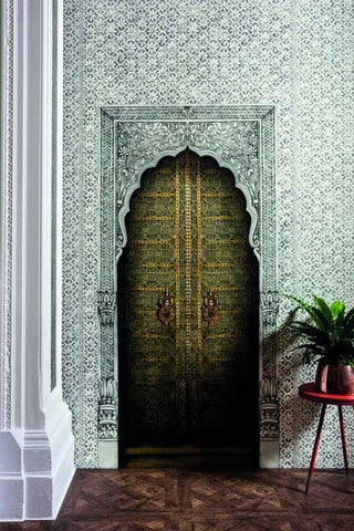 Image of a doorway with a decorative patterned wallpaper mural applied imitating an arched doorway, with a small table and plant to the right-hand side. 