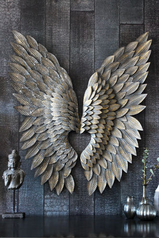 lifestyle image of the Beautiful Gold Angel Wings hung on black wood panel wall above black table with ornaments on