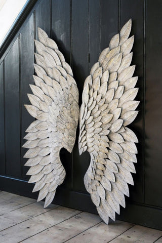 lifestyle image of feather effect metallic wings leaning on black wood panel wall and on wooden flooring