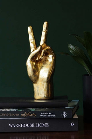 lifestyle image of gold peace hand ornament on pile of books with dark green wall background