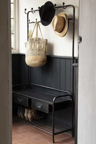 Lifestyle image of the Industrial-Style Hallway Storage Coat Rack with hats and bag hung on hooks and shoes on rack with dark panelled wood and white wall background