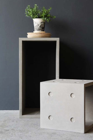 lifestyle image of Lyon Beton Concrete Dice StoolTable - Available In 2 Sizes one in front of the other with small plant in pot on top and dark wall background