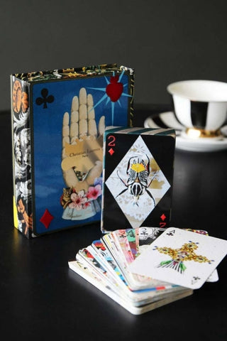 lifestyle image of maison de jeu by christian lacroix playing cards out of box on black table with black and white striped teacup and saucer