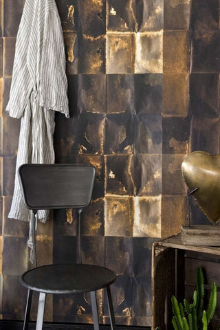 Lifestyle image of the Shibui wallpaper in copper in bathroom with black chair and white robe hanging on wall