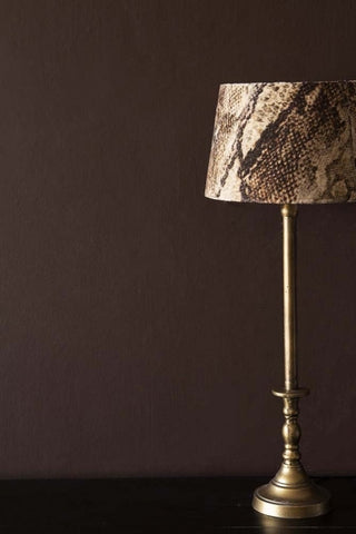 A gold table lamp with a snakeskin lampshade. The table lamp is in front of a wall painted in Briarwood paint, a dark brown paint. 