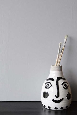 A quirky vase with a smiley face, sat in front of a wall painted in Gladstone Grey, a warm grey paint colour. 