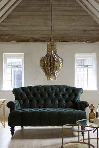 Lifestyle image of the Two-Seater Forest Green Velvet Sofa and Set Of 2 Circular Circus Nesting Tables and Shimmering Shell Disc Chandelier