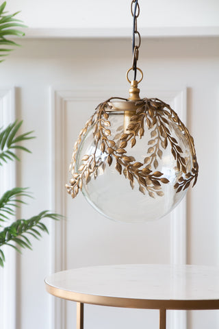 Lifestyle image of the Ornate Globe Pendant Ceiling Light With Brass Leaf Detailing with a table below