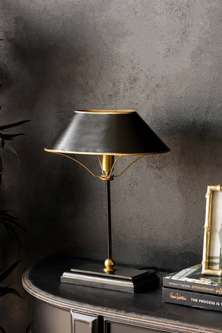 lifestyle image of black & gold table lamp on black table with dark wall background