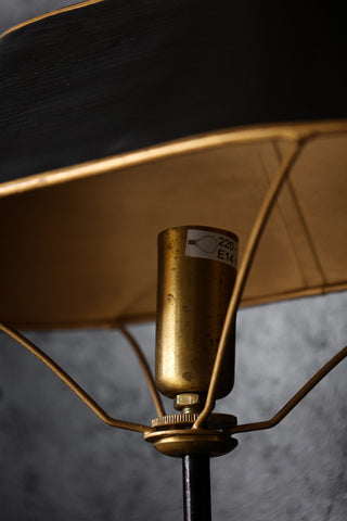 Detail image of black & gold table lamp on black table with dark wall background