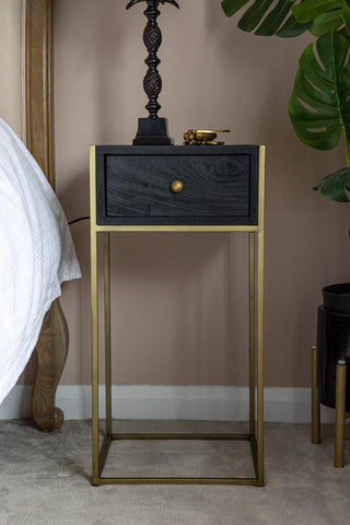 Lifestyle Image of the Black Wood & Brass Leg Bedside Table next to a bed with a lamp on top 