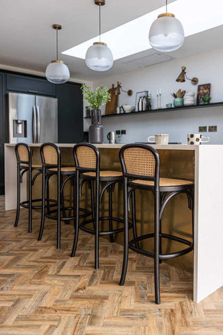 A wide image of a row of the Chez Pitou Black Wood & Woven Cane Bar Stool in a kitchen