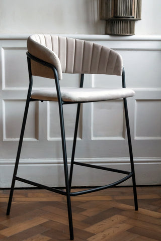 Lifestyle image of the Curved Back Velvet Bar Stool In Mink Grey against a white pannelled wall
