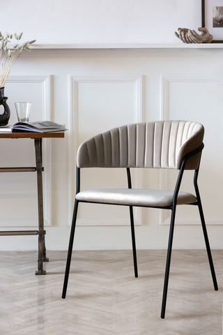 Lifestyle image of Curved Back Velvet Dining Chair In Mink Grey with panelled wall facing left