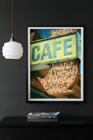 Lifestyle image of the Cafe Art Print on a dark wall with books on black table and white hanging light
