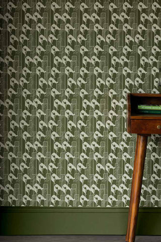 Image showing green and white printed wallpaper of female figure and architecture, displayed on a wall alongside a wooden side table. 