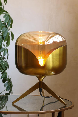 Lifestyle image of the Retro Golden Glass Tripod Table Lamp lit up