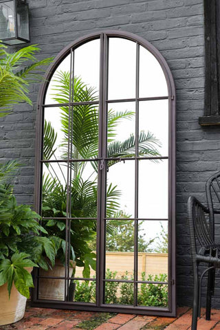 Image of the Tall Black Arch Indoor/Outdoor Window Pane Mirror With Opening Doors in the garden