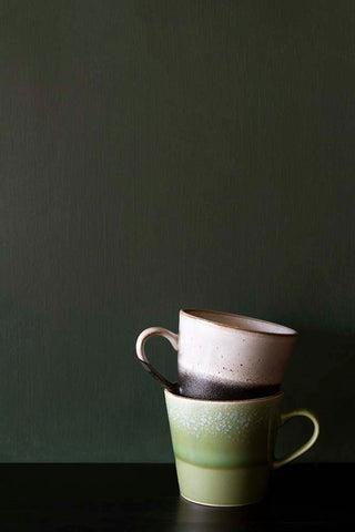 Two earthenware mugs stacked on top of each other, shot in front of a wall in Juniper leaf, a warm deep green paint. 