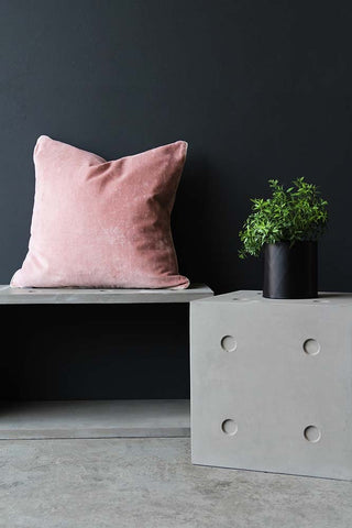 lifestyle image of Lyon Beton Concrete Dice StoolTable - Available In 2 Sizes with pink pillow and plant in pot on top with dark wall background