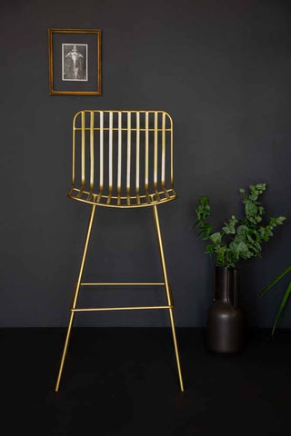 front on angle lifestyle image of the midas bar stool with plants and black flooring and copper picture frame on dark wall background