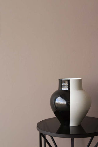 A large black and white vase  photographed in front of a wall painted in Rockett St George Broderie paint, this paint is a warm pink, natural colour.