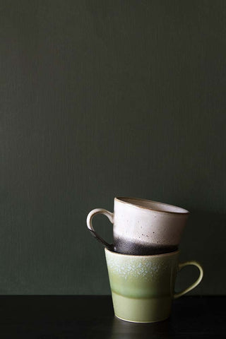 Two ceramic cups stacked on top of each other, photographed in front of a wall painted in Juniper leaf, a dark green paint. 