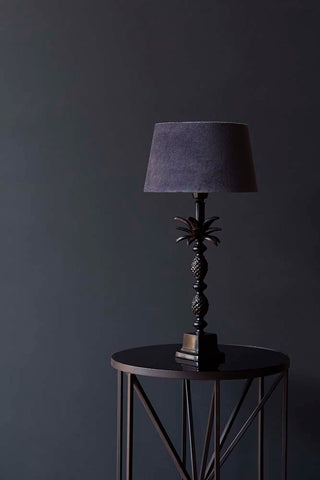 A black palm tree table lamp on a black table photographed in front of a wall painted in Portobello pain, a Rockett St George paint in dark grey / black.