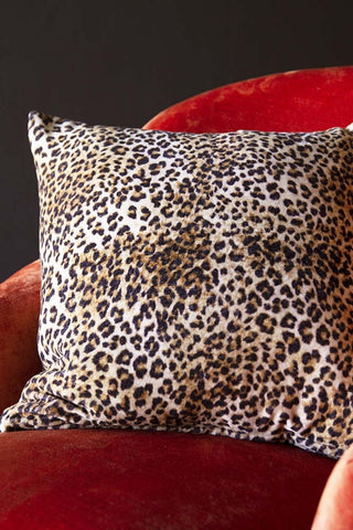 Image showing a leopard print square cushion, displayed on a red velvet chair.