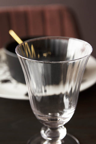 Close-up detail image of the Ribbed Glass Wine Glass on black table with tableware behind and red velvet chair