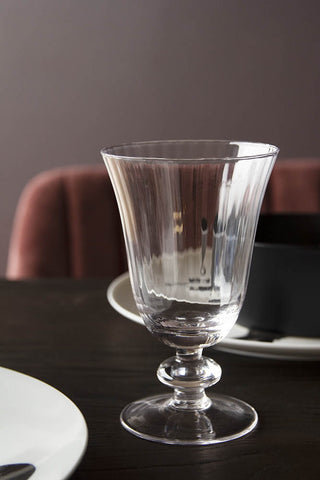 Lifestyle image of the Ribbed Glass Wine Glass on black table with velvet chair in background with dark wall 